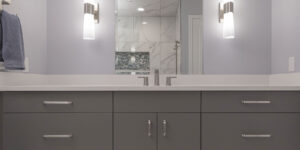 Image of a remodeled bathroom showing a vanity with sink, quartz countertop, mirror, and lighting.